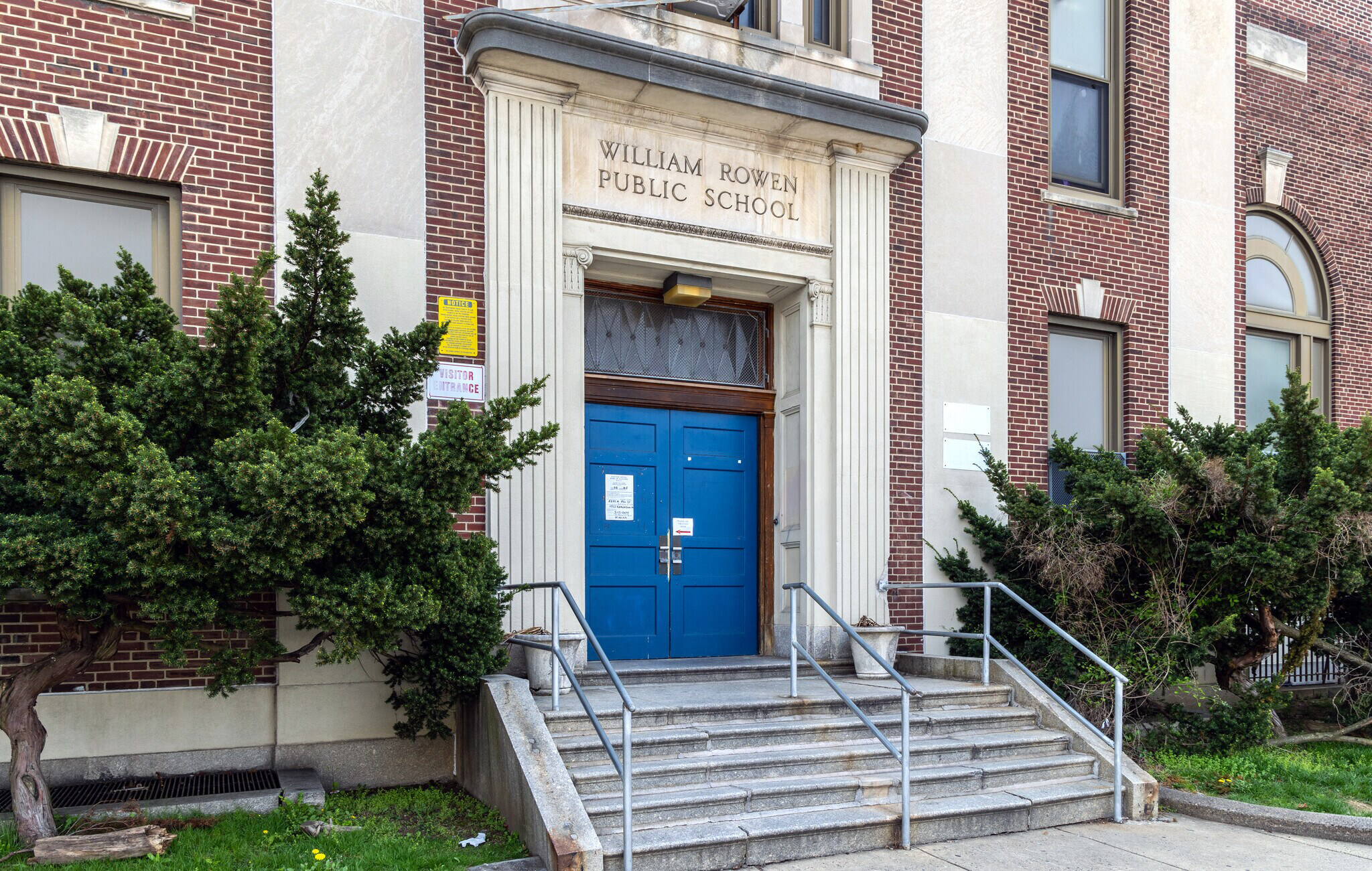 Front entrance of William Rowen Elementary School featuring blue double doors, brick walls and concrete steps.